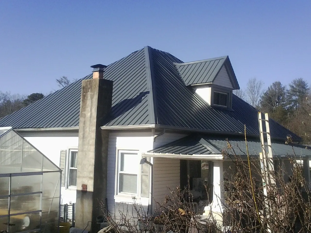 Dark blue standing seam metal roof on a white farmhouse with dormer — Slate & Tile Roof Repair by Roofing Brothers in Avon