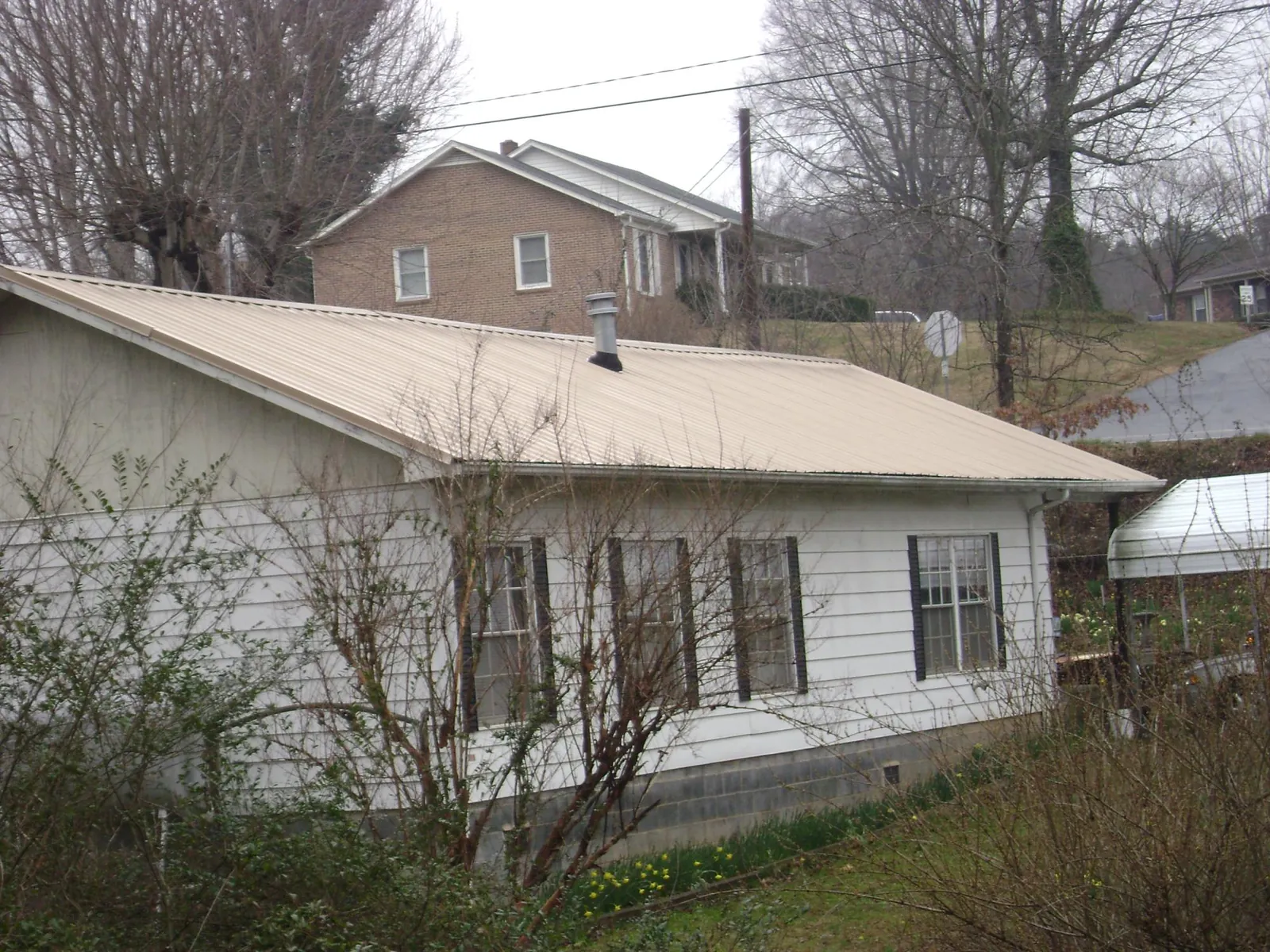 Tan metal roof on a white sided house set into a hillside — Commercial Roofing by Roofing Brothers in Avon
